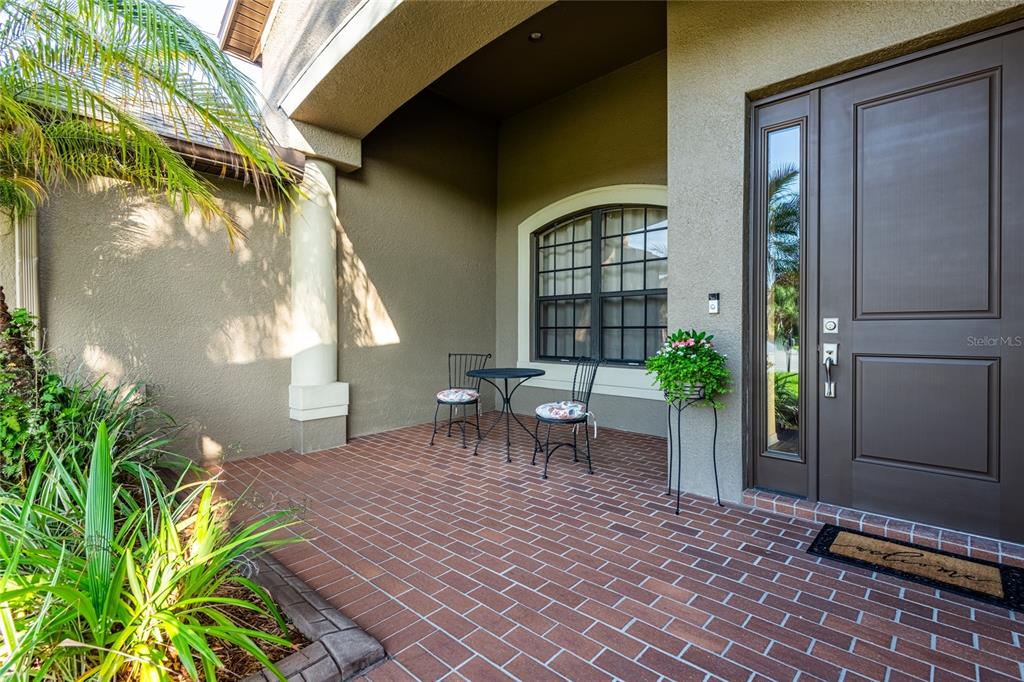 A covered brick patio features a small bistro set and a front door entrance — 14815 NINEBARK COURT, LAND O LAKES, FL