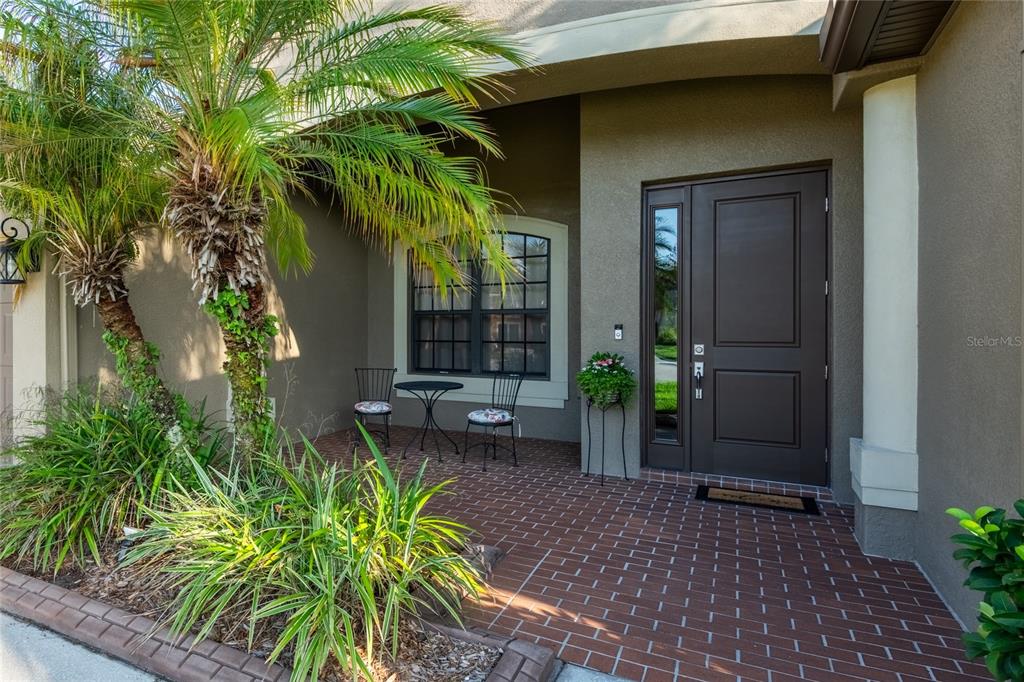 A front porch with brick flooring, a dark brown door, and a small bistro set — 14815 NINEBARK COURT, LAND O LAKES, FL