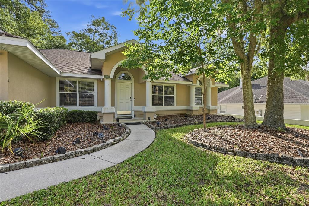 A tan single-story house with a curved walkway, arched entryway, and mature trees in front — 1003 NW 106TH STREET, GAINESVILLE, FL
