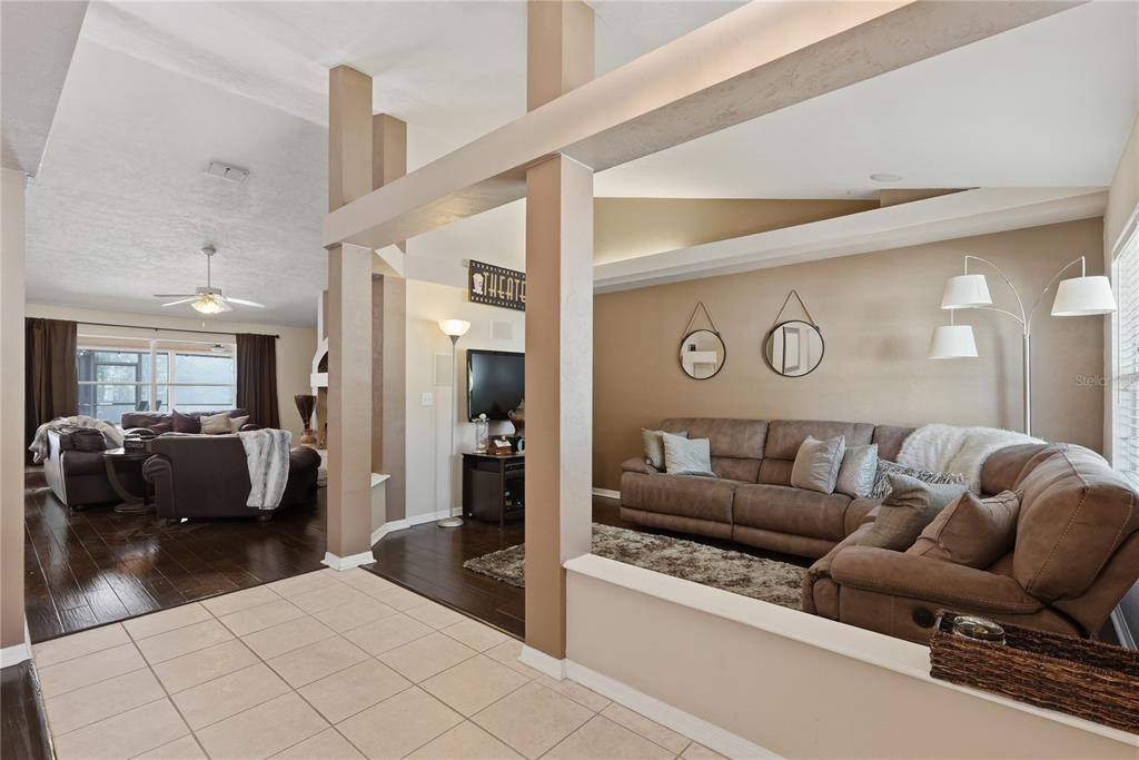 A living room with brown sectional sofas, hardwood floors, and a partial wall divider — 1003 NW 106TH STREET, GAINESVILLE, FL