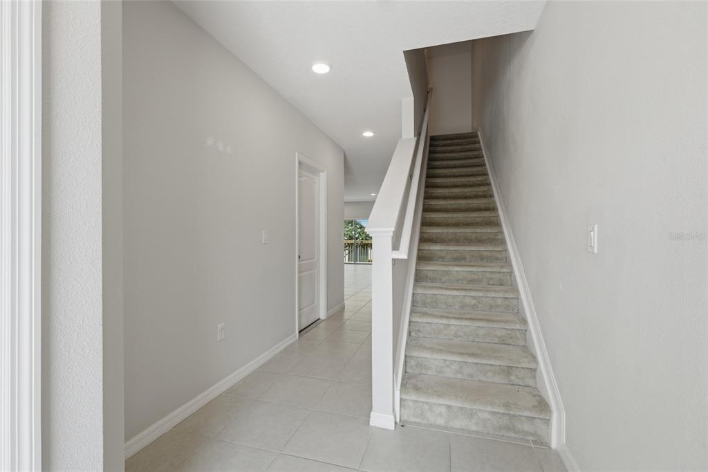 A hallway with tile flooring leads to a carpeted staircase and a doorway — 3857 HAMPSTEAD LANE, LAKELAND, FL