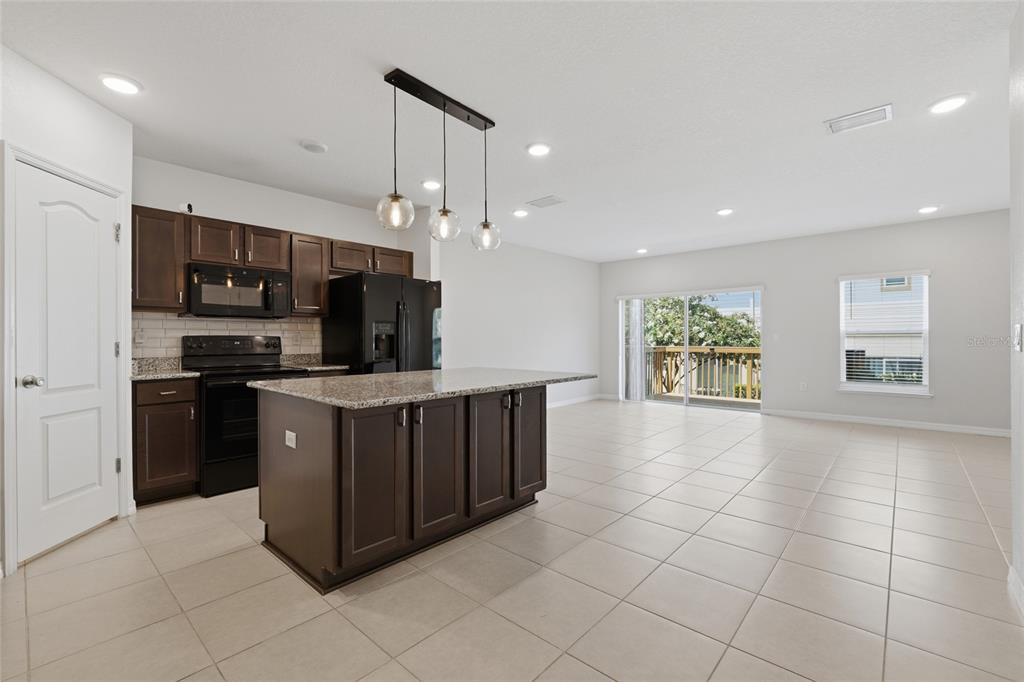 A kitchen with dark wood cabinets, granite countertops, and an island opens to a living area — 3857 HAMPSTEAD LANE, LAKELAND, FL