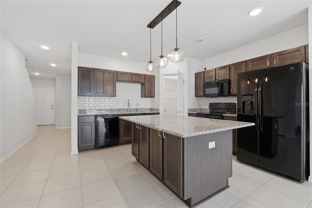 A kitchen features dark wood cabinets, granite countertops, a central island, and black appliances — 3857 HAMPSTEAD LANE, LAKELAND, FL