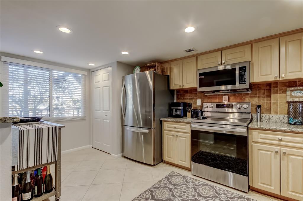 A kitchen features stainless steel appliances, light wood cabinets, granite countertops, and tile flooring — 650 ISLAND WAY UNIT 206, CLEARWATER BEACH, FL