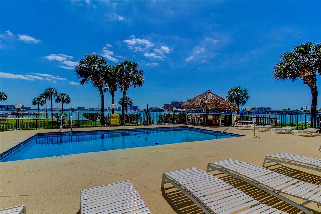 An outdoor swimming pool with lounge chairs and a tiki bar overlooking the water — 650 ISLAND WAY UNIT 206, CLEARWATER BEACH, FL