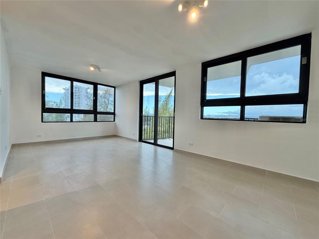 An empty room features light-colored tile floors, large windows, and a glass door to a balcony — 1 CALLE INGA UNIT 8D, SAN JUAN, PR