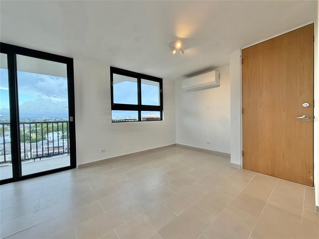 An empty room features light tile flooring, a sliding glass door, a window, and air conditioning — 1 CALLE INGA UNIT 8D, SAN JUAN, PR