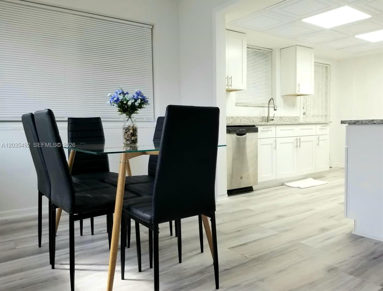 A galley kitchen features white cabinets, granite countertops, stainless steel appliances, and light wood flooring — 1601 Bay Rd # 7, Miami Beach FL 33139, MIAMI BEACH, FL