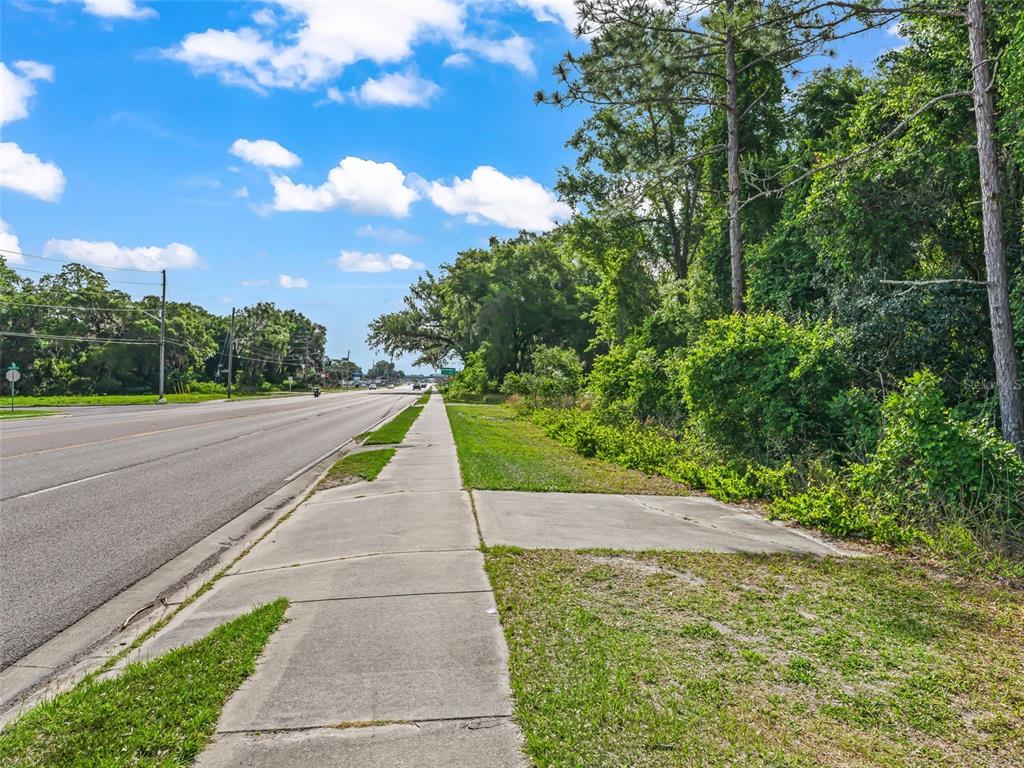 A sidewalk runs alongside a paved road next to a wooded area under a blue sky — 2823 W C 48, BUSHNELL, FL