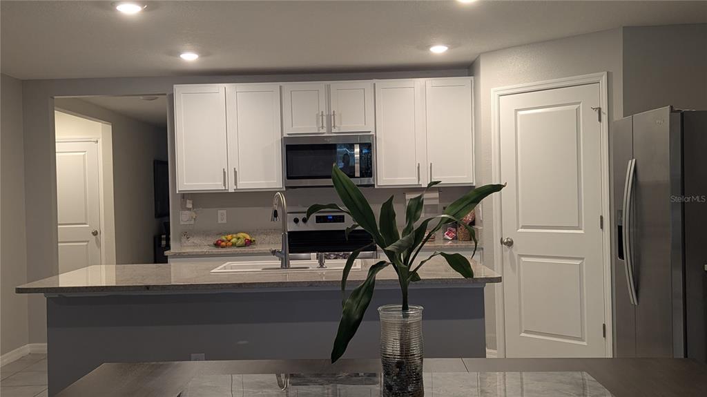 A kitchen features white cabinets, granite countertops, a stainless steel refrigerator, and a center island — 3719 CAPRI COAST DRIVE, PLANT CITY, FL