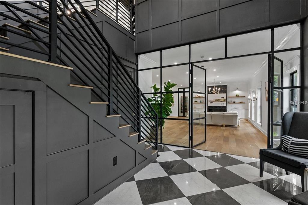 A staircase with dark paneling and railings overlooks a room with glass-paned walls and floors — 3501 W TACON STREET, TAMPA, FL