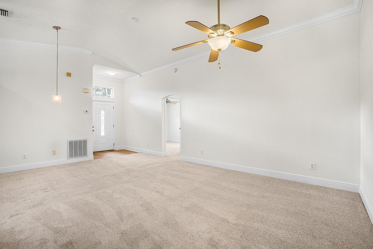 An empty living room features beige carpeting, white walls, a ceiling fan, and a front door — 966 E 13th Square, Vero Beach FL 32960, VERO BEACH, FL
