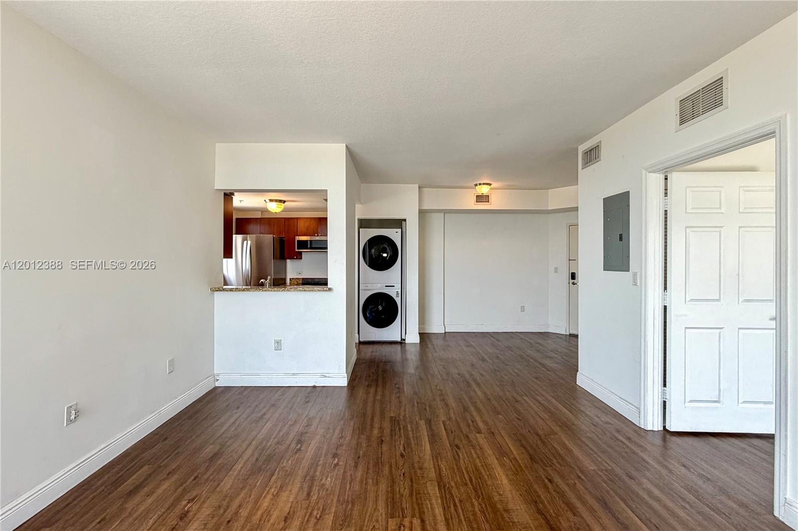 An open living area features wood-look flooring, a kitchen pass-through, and a stacked laundry unit — 2600 SW 27th Ave # 902, Miami FL 33133, MIAMI, FL