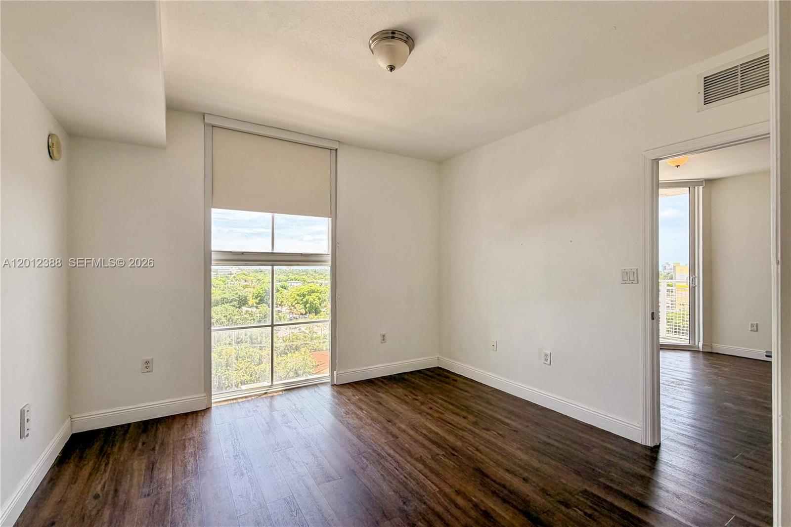An empty room features dark wood-look flooring, white walls, and a large window with views — 2600 SW 27th Ave # 902, Miami FL 33133, MIAMI, FL