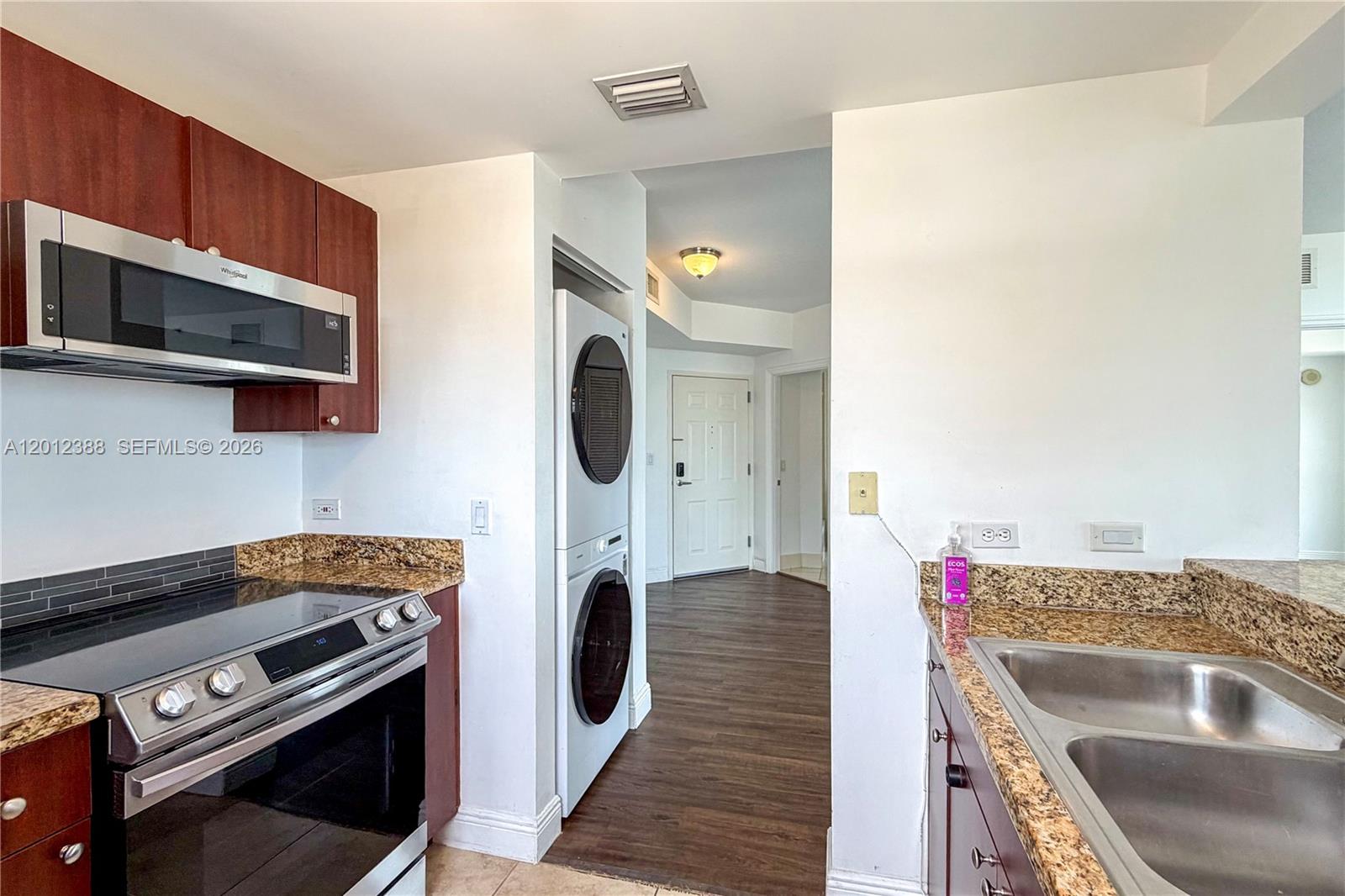A kitchen features dark wood cabinets, granite countertops, stainless steel appliances, and a stacked washer-dryer — 2600 SW 27th Ave # 902, Miami FL 33133, MIAMI, FL