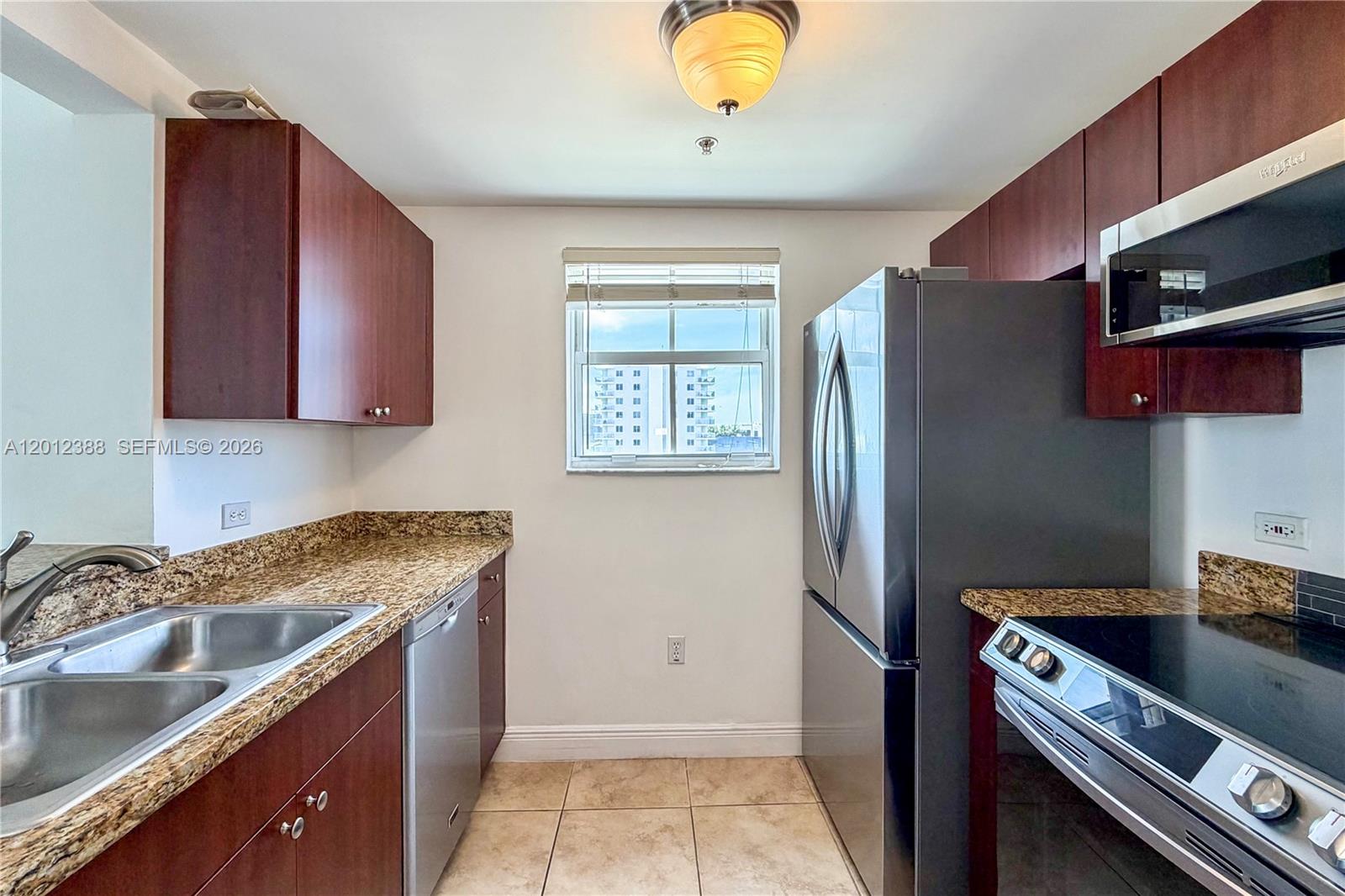 A galley kitchen features dark wood cabinets, granite countertops, stainless steel appliances, and tile flooring — 2600 SW 27th Ave # 902, Miami FL 33133, MIAMI, FL