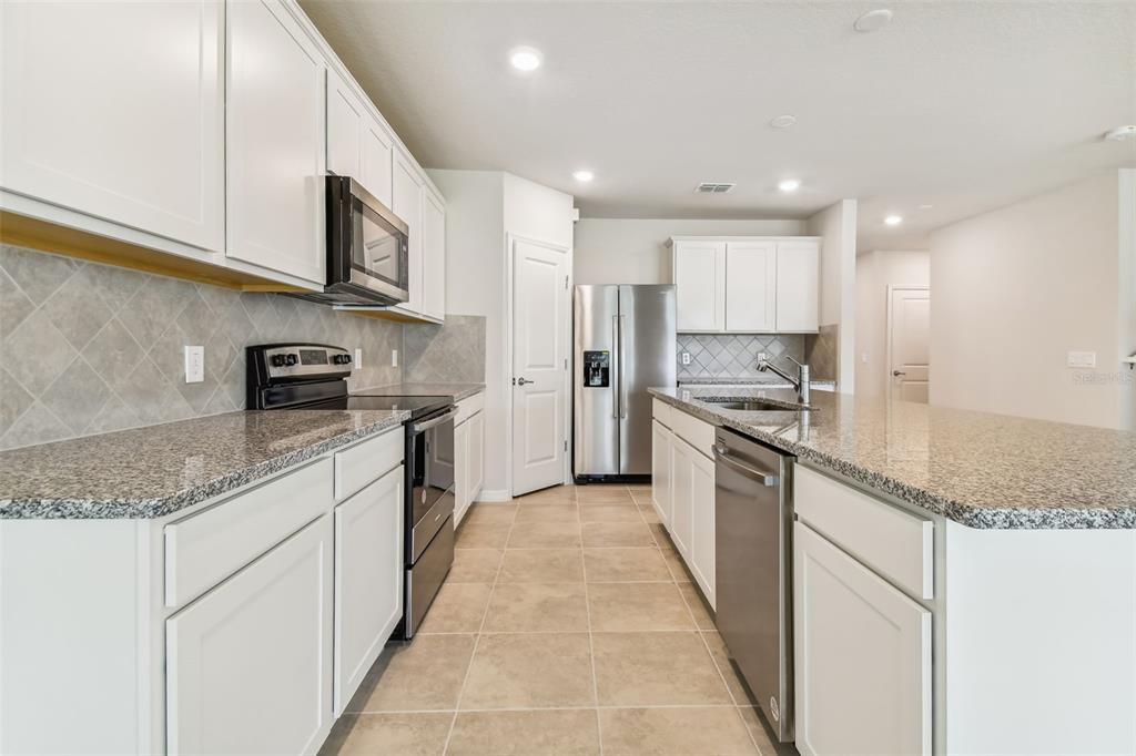 A kitchen with white cabinets, granite countertops, stainless steel appliances, and tile flooring — 13718 EVERGREEN VALLEY DRIVE, RIVERVIEW, FL