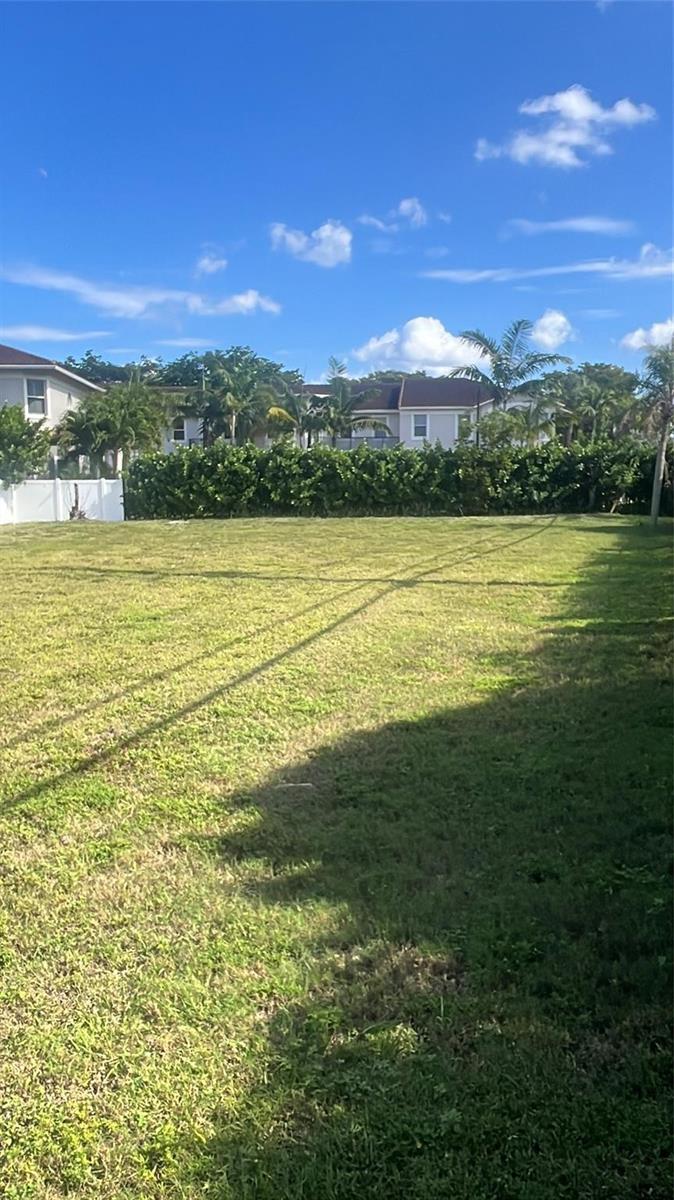 A grassy, vacant residential lot features a hedge and palm trees against a blue sky — 1855 Copley Place, Delray Beach FL 33445, DELRAY BEACH, FL