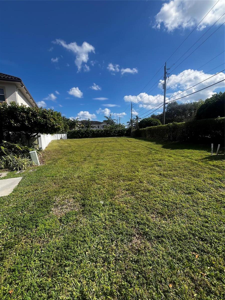 A large, grassy vacant lot is bordered by a white fence and tall green hedges — 1855 Copley Place, Delray Beach FL 33445, DELRAY BEACH, FL