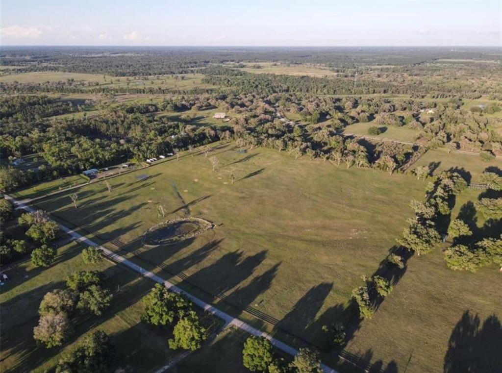 An aerial view shows a large, grassy pasture with scattered trees and a small pond — NW 160 AVENUE, MORRISTON, FL