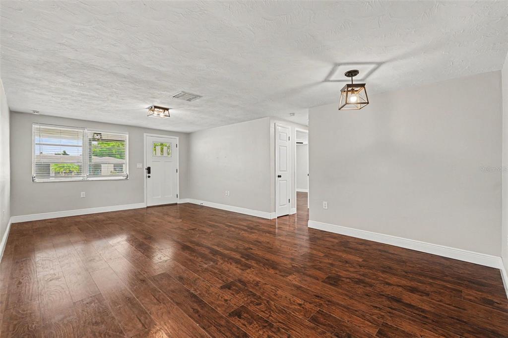 An empty living room features dark wood flooring, light gray walls, and two ceiling lights — 6244 6TH AVENUE, NEW PORT RICHEY, FL