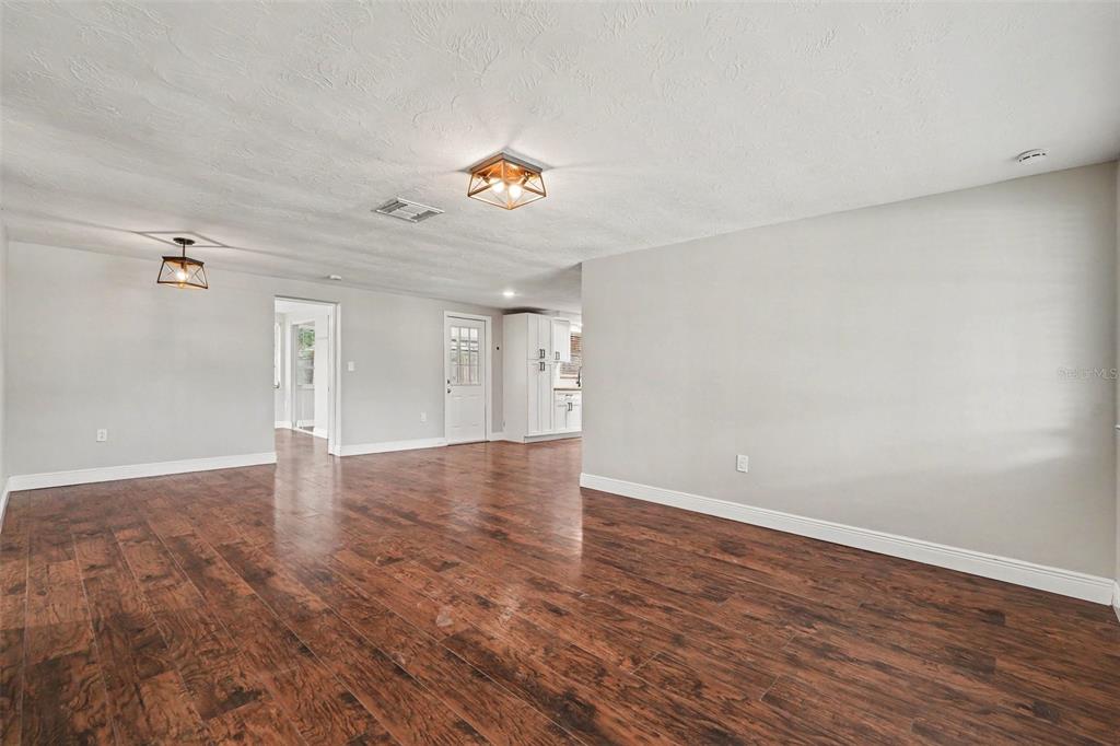 An open-concept living area features dark wood-look flooring, light gray walls, and two ceiling lights — 6244 6TH AVENUE, NEW PORT RICHEY, FL