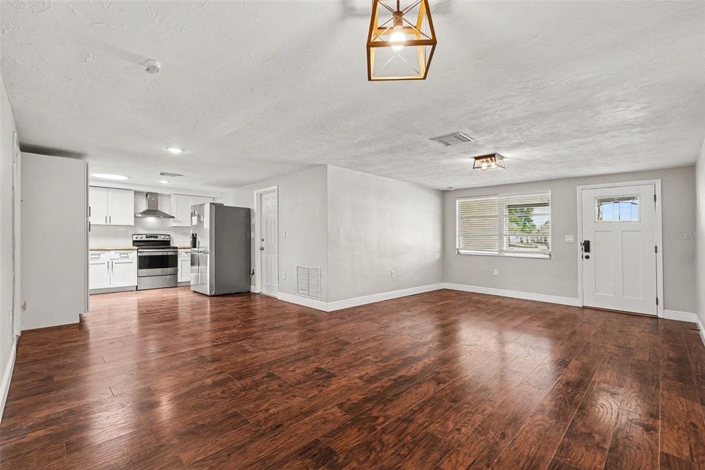 An open-concept living area with wood-look flooring, white walls, and an adjacent kitchen — 6244 6TH AVENUE, NEW PORT RICHEY, FL