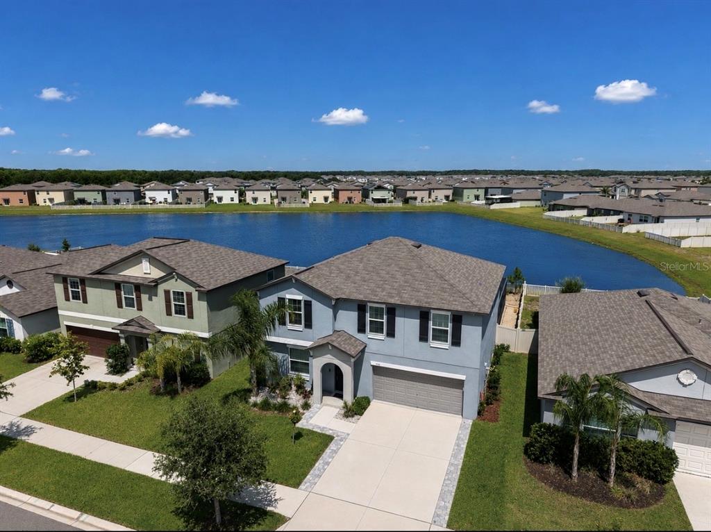 An aerial view shows two-story suburban houses with attached garages facing a large retention pond — 5519 BLUE AZURE DRIVE, WIMAUMA, FL
