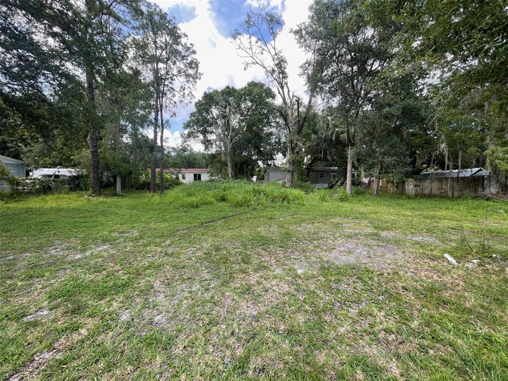 A grassy, vacant lot surrounded by mature trees and neighboring residential structures — 18533 16TH AVENUE, ORLANDO, FL