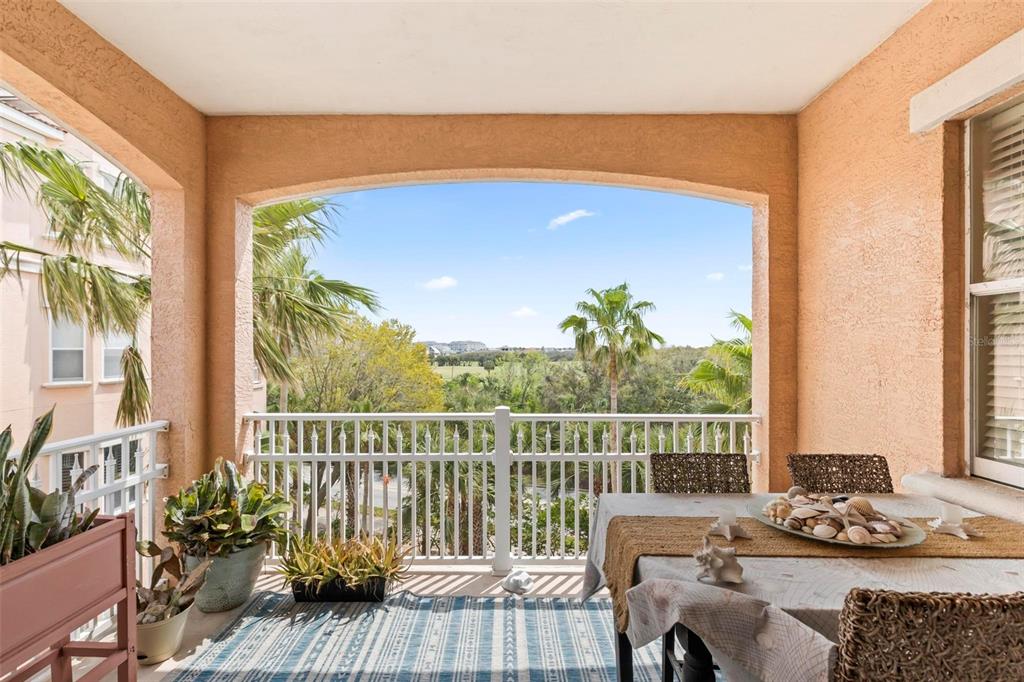 A covered balcony features a dining table, potted plants, and a view of palm trees — 35 OCEAN CREST WAY UNIT 1135, PALM COAST, FL