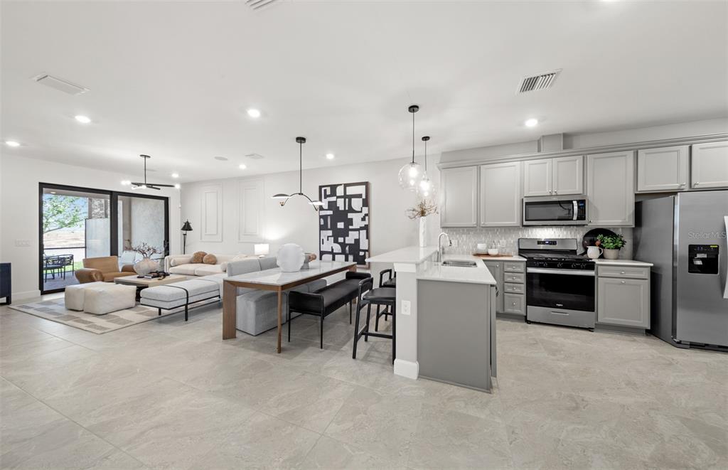 An open-concept kitchen and living area features gray cabinetry, tile flooring, and a dining table — 18809 INDIAN ROCK PLACE, LAKEWOOD RANCH, FL