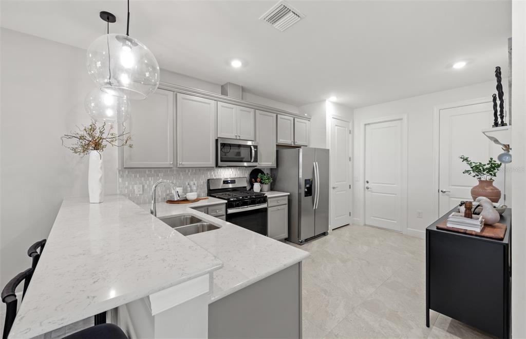 A kitchen features gray cabinets, stainless steel appliances, and a white quartz breakfast bar — 18809 INDIAN ROCK PLACE, LAKEWOOD RANCH, FL