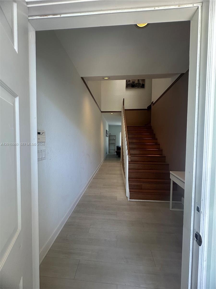 A narrow entryway features light wood-look flooring, white walls, and a wooden staircase — 5402 Pointe Villa Dr # B, Lighthouse Point FL 33064, LIGHTHOUSE POINT, FL