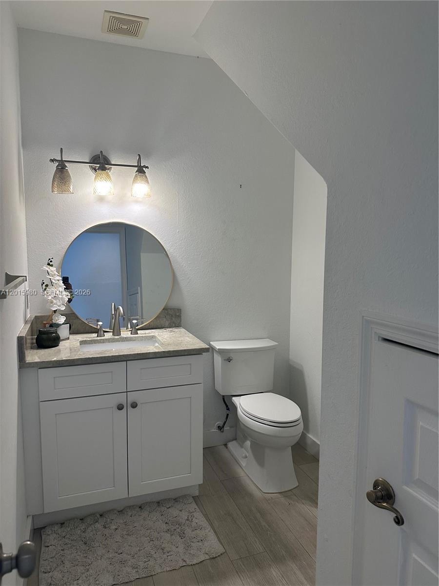 A small bathroom features a white vanity, a round mirror, and a toilet — 5402 Pointe Villa Dr # B, Lighthouse Point FL 33064, LIGHTHOUSE POINT, FL