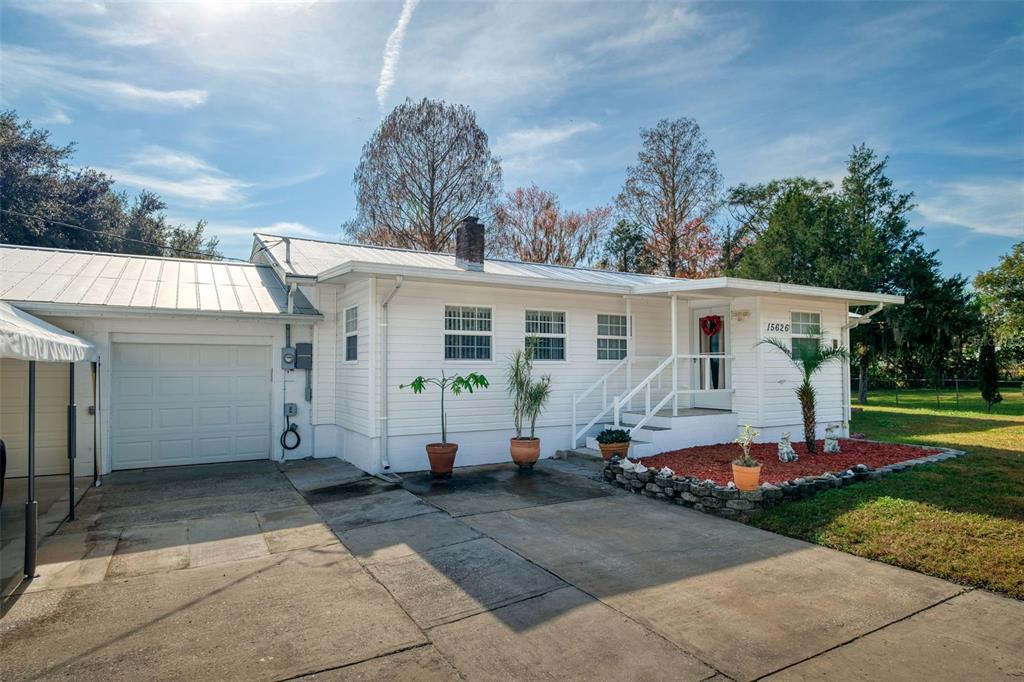 A white single-story house with a metal roof, attached garage, and a concrete driveway — 15626 LARKSPUR STREET, ORLANDO, FL