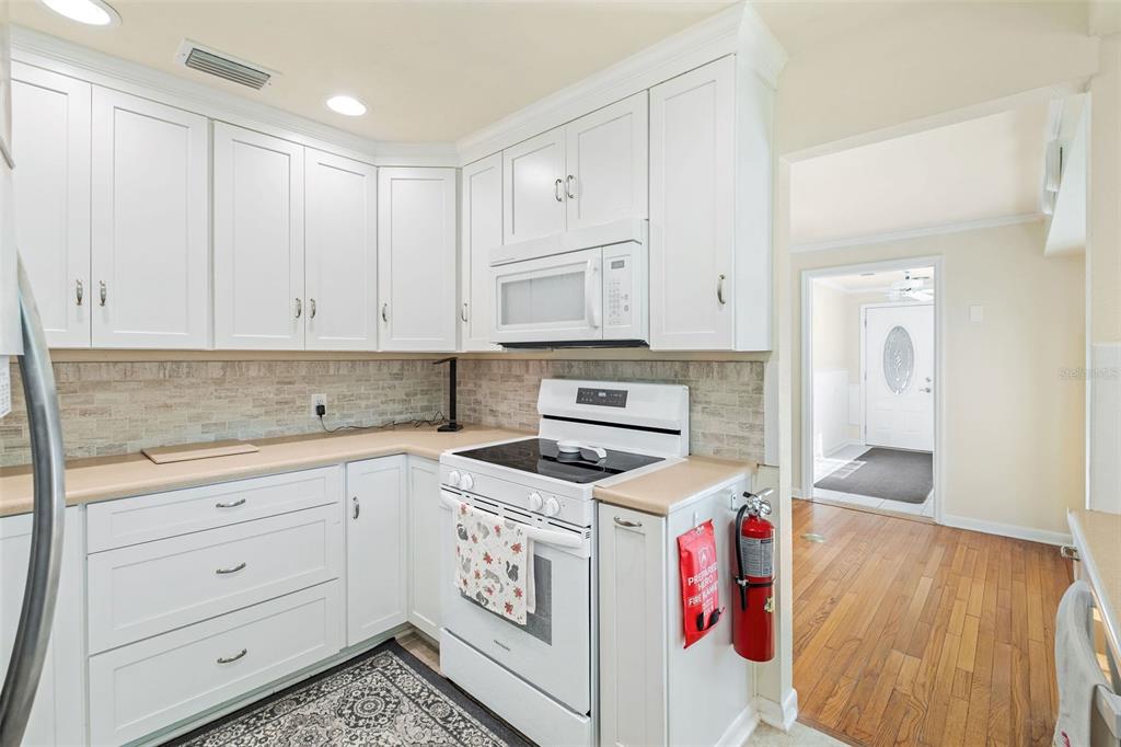 A kitchen with white cabinets, tan countertops, a white stove, and a fire extinguisher — 15626 LARKSPUR STREET, ORLANDO, FL