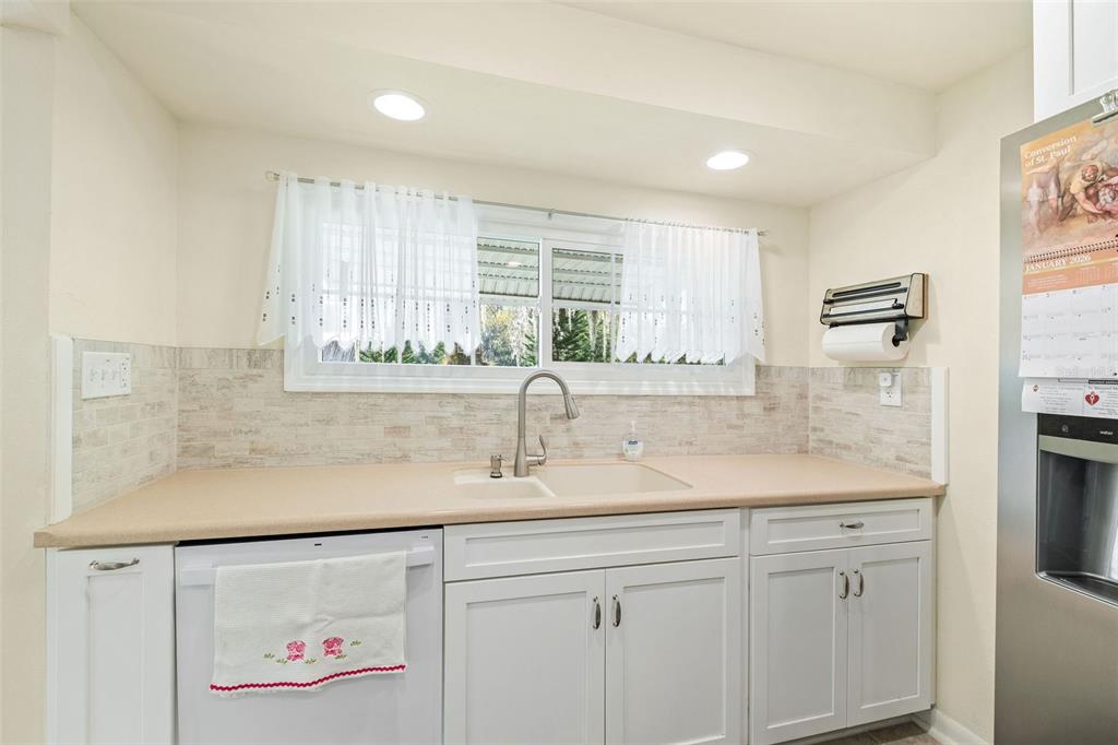 A kitchen features white cabinets, a beige countertop, a double sink, and a tiled backsplash — 15626 LARKSPUR STREET, ORLANDO, FL