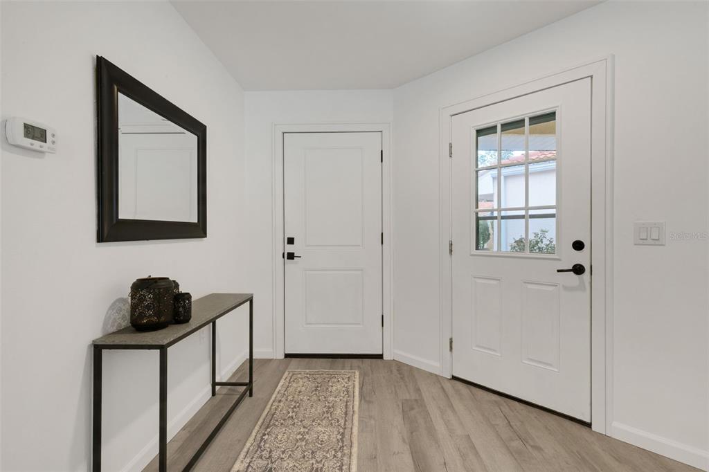 An entryway features light wood-look flooring, white walls, a console table, and two white doors — 606 MARCUS STREET UNIT 26, VENICE, FL