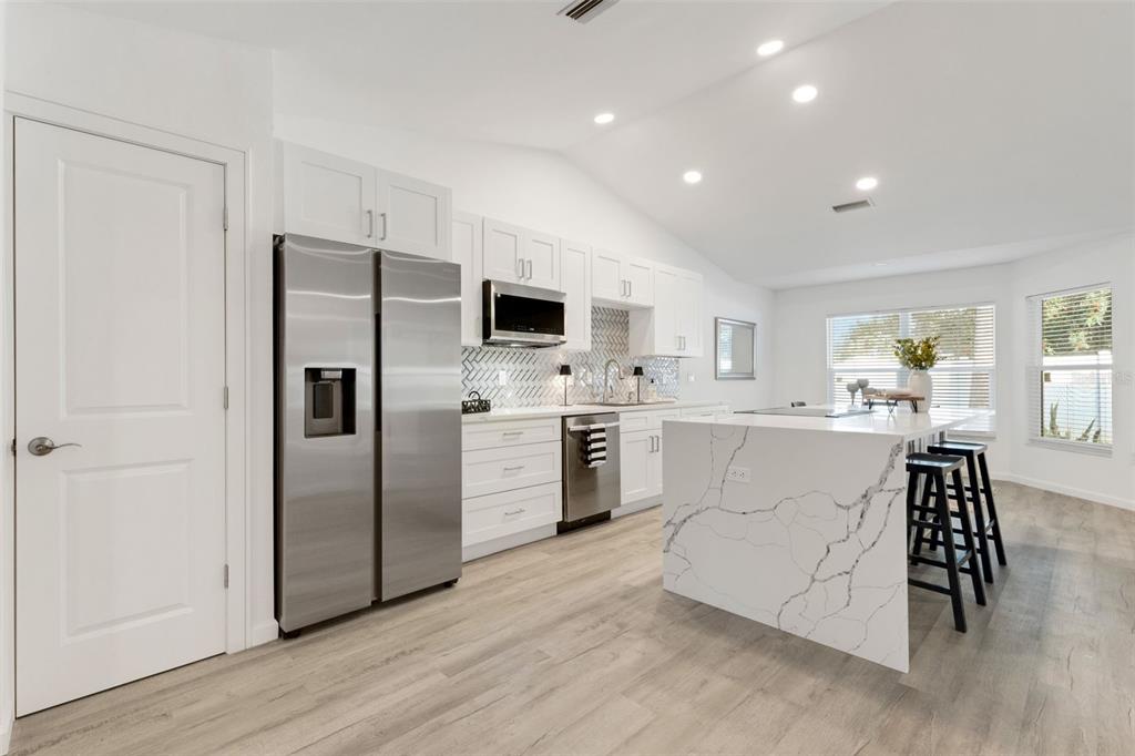 A modern kitchen features white cabinetry, stainless steel appliances, and a marble-patterned waterfall island — 606 MARCUS STREET UNIT 26, VENICE, FL