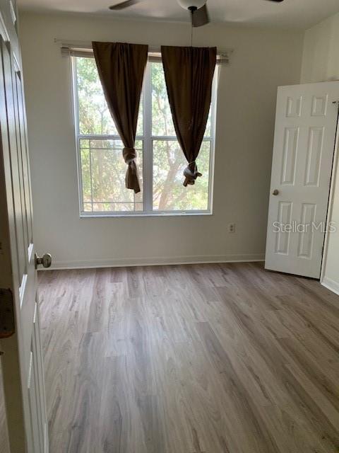 An empty bedroom features light wood-look flooring, a ceiling fan, and a window with curtains — 4247 TYLER CIRCLE N, ST PETERSBURG, FL