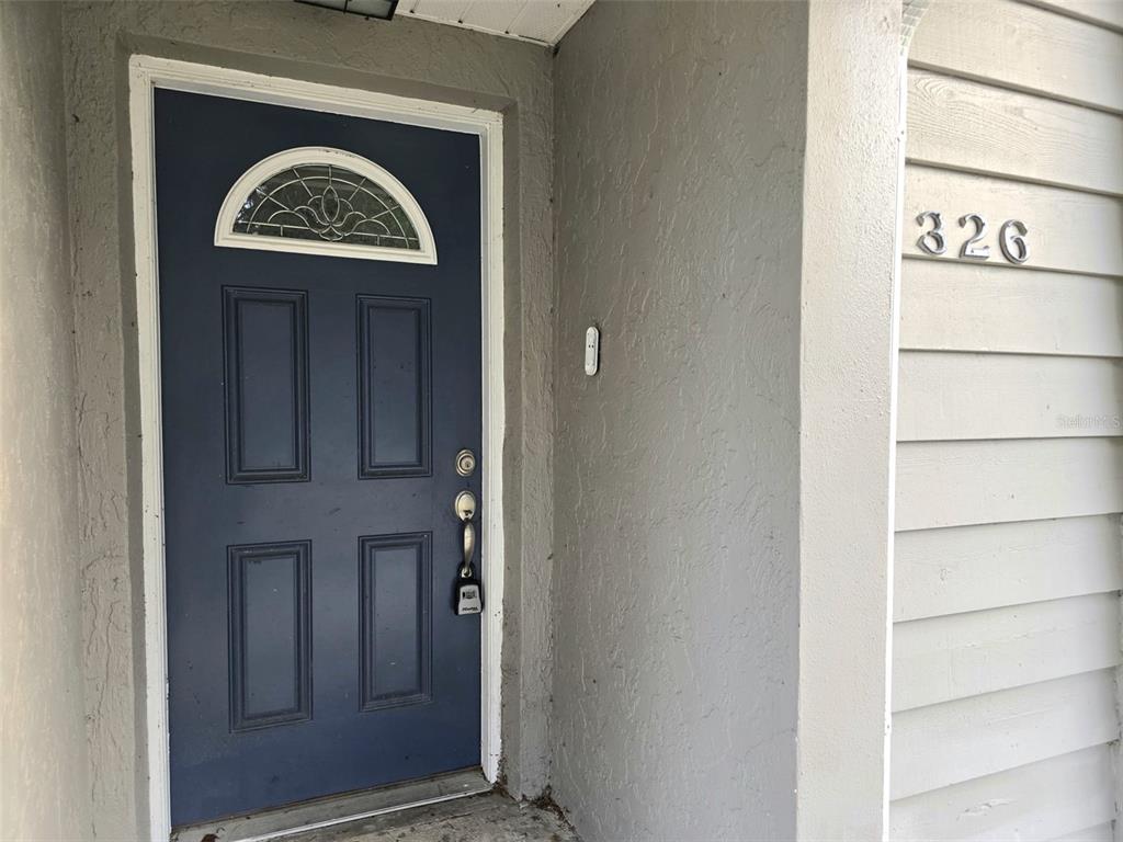 A dark blue front door with a decorative window sits beside a gray exterior wall — 326 COLONADE COURT, KISSIMMEE, FL