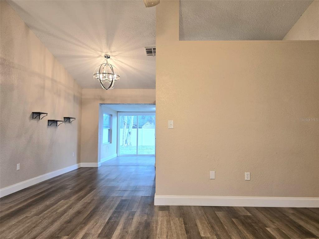 A living area with wood-look flooring, a chandelier, and a view into a sunroom — 326 COLONADE COURT, KISSIMMEE, FL