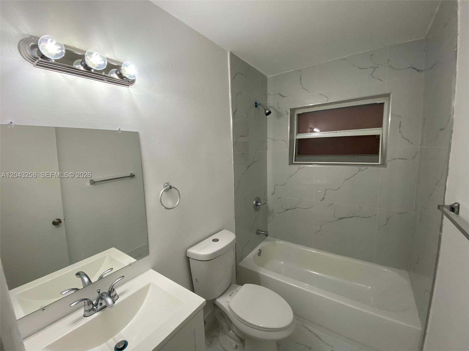 A bathroom features a white vanity, a toilet, and a bathtub with marble-patterned tile walls — 1842 Madison St # 3, Hollywood FL 33020, HOLLYWOOD, FL