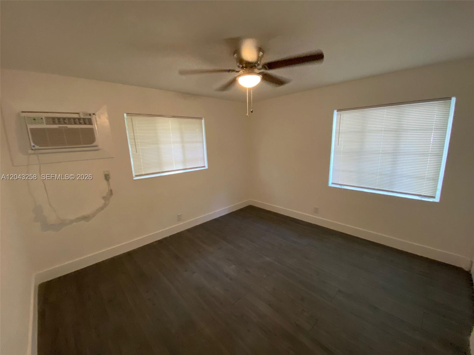 An empty bedroom features dark wood-look flooring, white walls, a ceiling fan, and a window unit — 1842 Madison St # 3, Hollywood FL 33020, HOLLYWOOD, FL