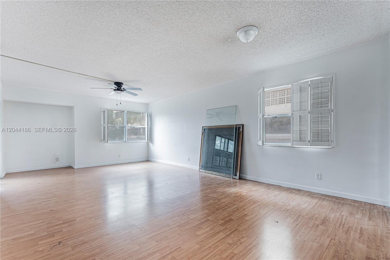 A bright, empty living room features light wood-look flooring, white walls, and two windows — 3301 Spanish Moss Ter # 406, Lauderhill FL 33319, LAUDERHILL, FL
