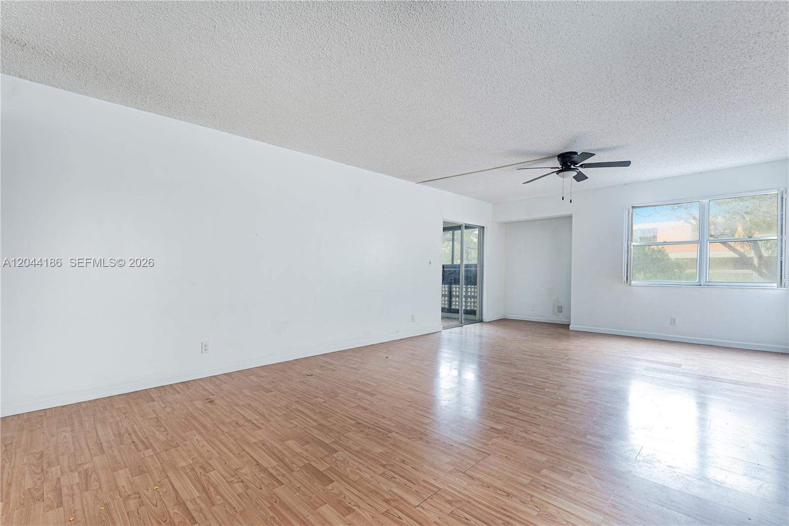 An empty living room features white walls, wood-look laminate flooring, and a ceiling fan — 3301 Spanish Moss Ter # 406, Lauderhill FL 33319, LAUDERHILL, FL
