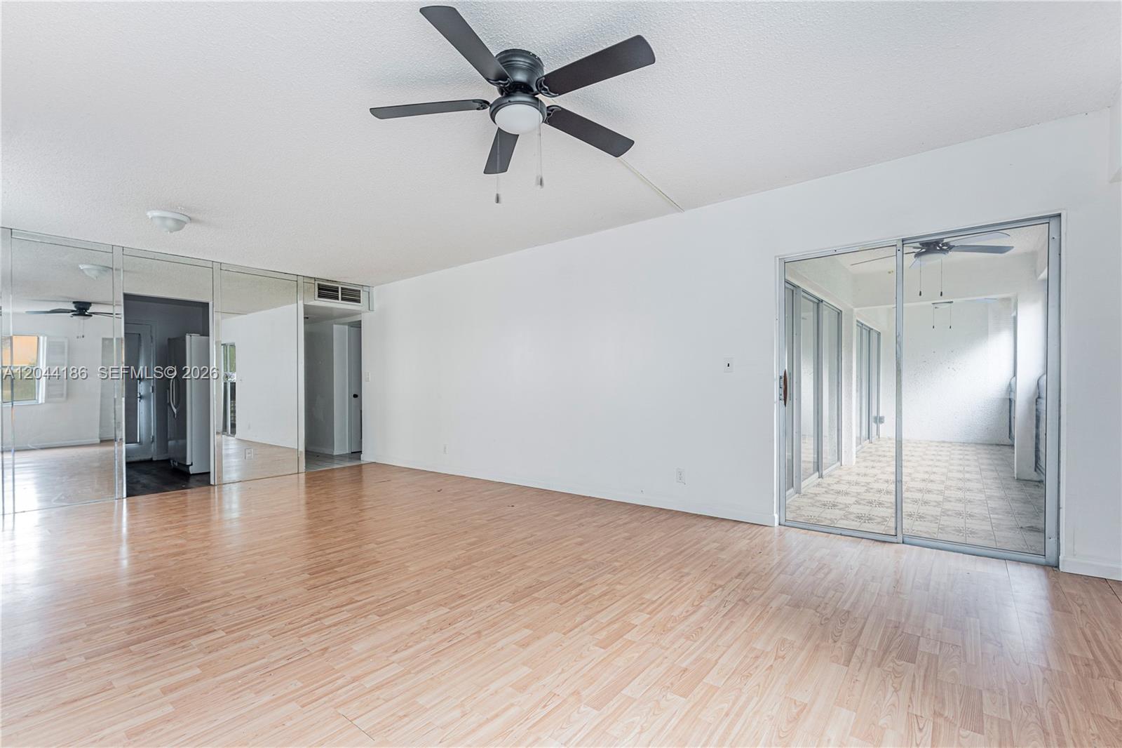 An empty living room features wood-look flooring, a ceiling fan, mirrored walls, and sliding doors — 3301 Spanish Moss Ter # 406, Lauderhill FL 33319, LAUDERHILL, FL