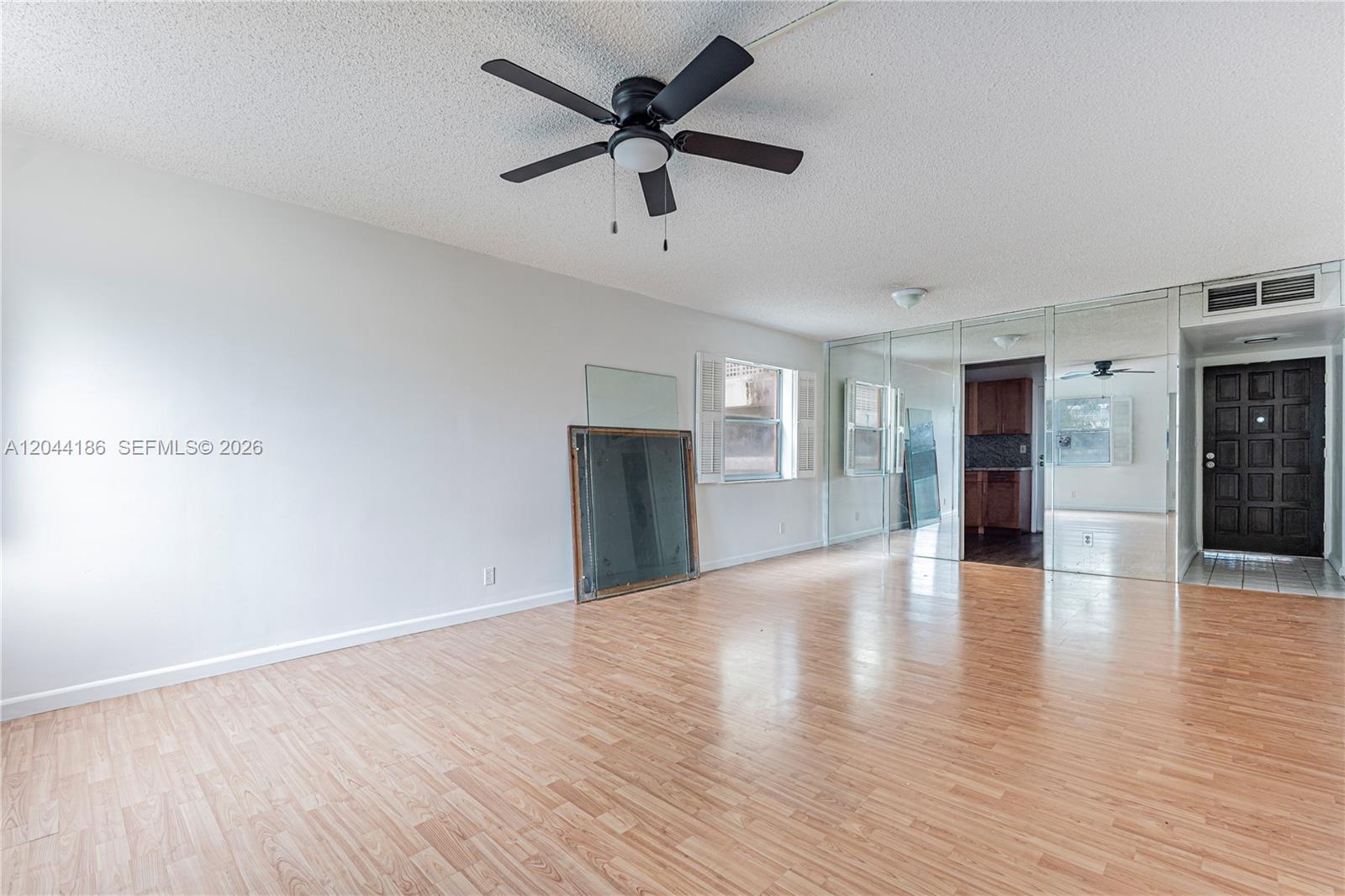 A living room features light wood flooring, a ceiling fan, and mirrored wall panels — 3301 Spanish Moss Ter # 406, Lauderhill FL 33319, LAUDERHILL, FL