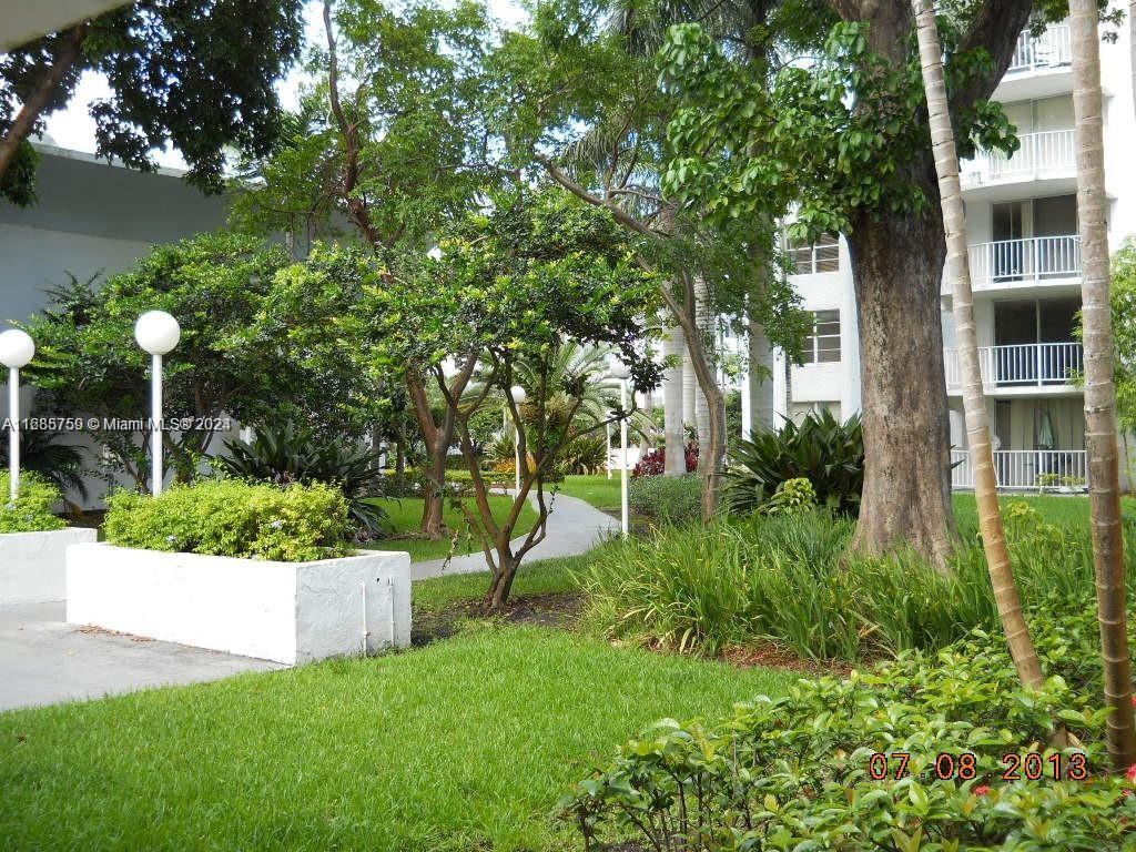 A paved walkway winds through a landscaped courtyard with trees, shrubs, and white apartment buildings — 498 NW 165th St Rd # 607, Miami FL 33169, MIAMI, FL
