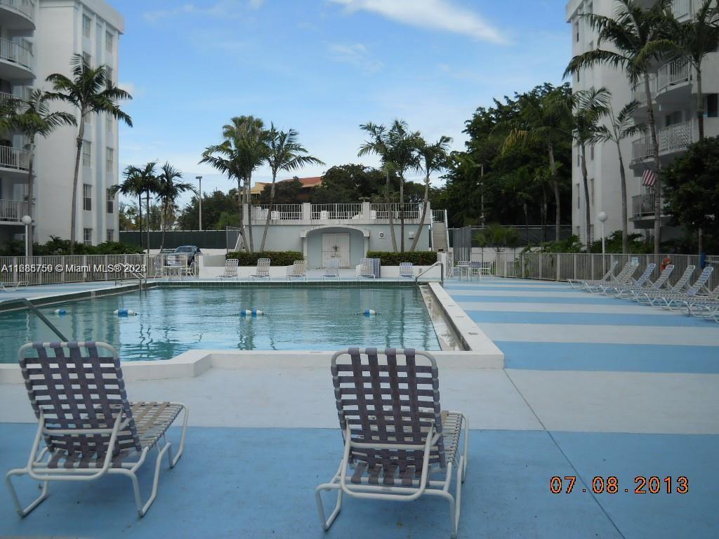 An outdoor swimming pool is surrounded by lounge chairs and palm trees between two buildings — 498 NW 165th St Rd # 607, Miami FL 33169, MIAMI, FL